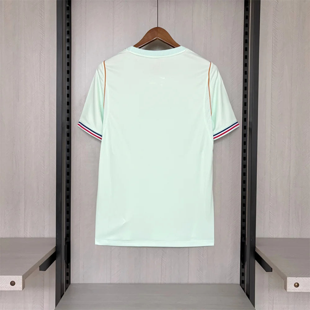 Light green t-shirt with red and blue stripes on a hanger against a neutral background