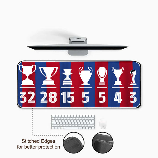Desk setup with a large mouse pad featuring trophy designs and numbers, keyboard, and mouse on a white background.