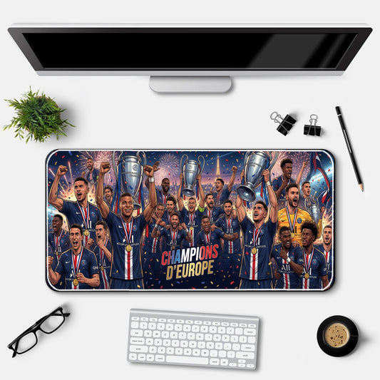 Desk setup with a large mouse pad featuring a soccer team celebrating with trophies, a computer monitor, keyboard, and office supplies.