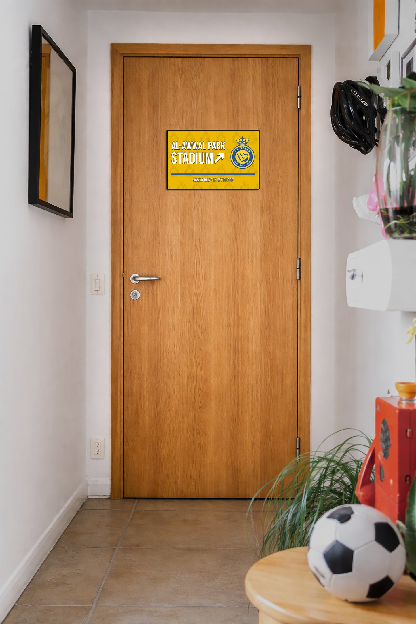 Wooden door with a yellow sign in a hallway with a soccer ball and plant on a table.