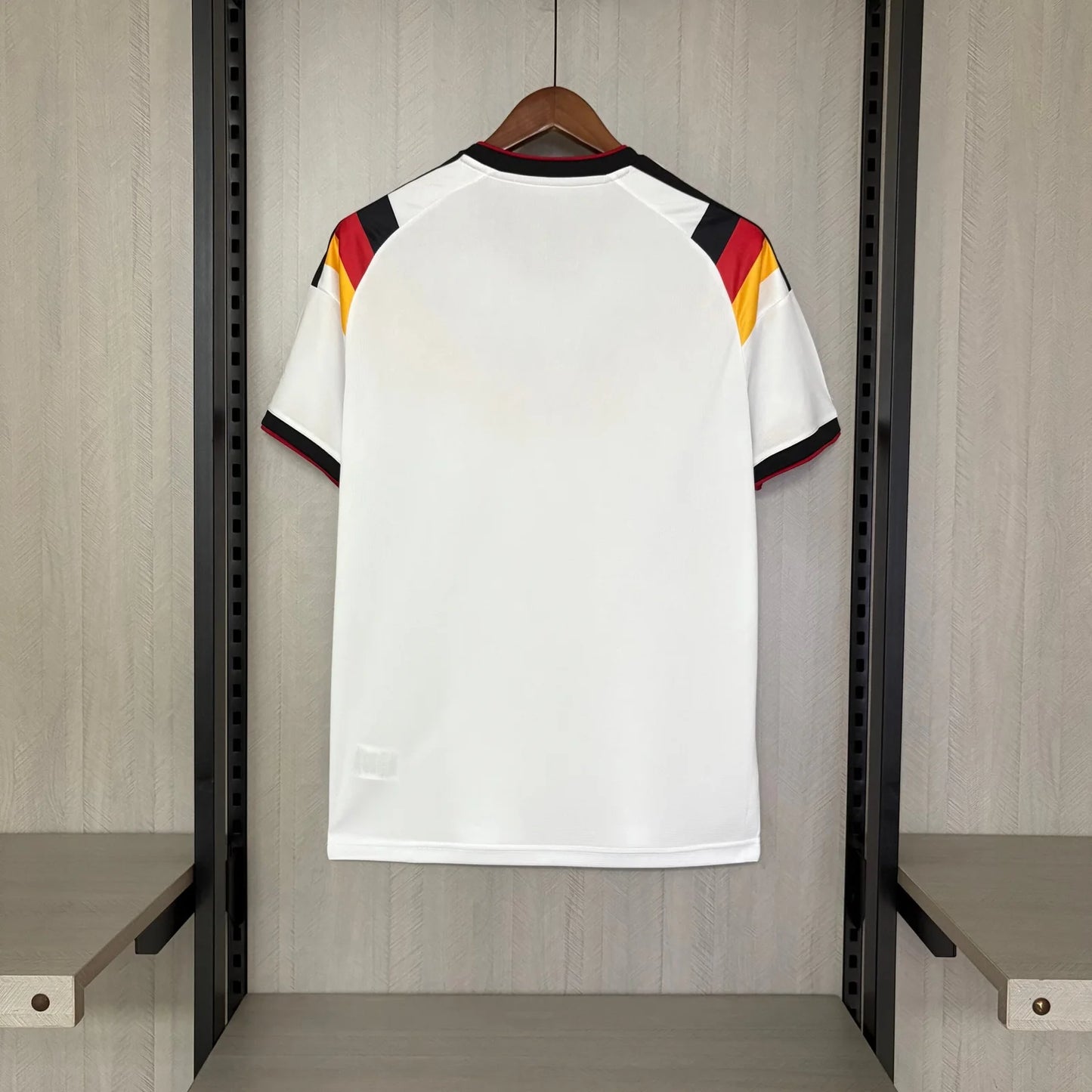 White sports jersey with red, yellow, and black accents on a hanger against a wooden panel background.