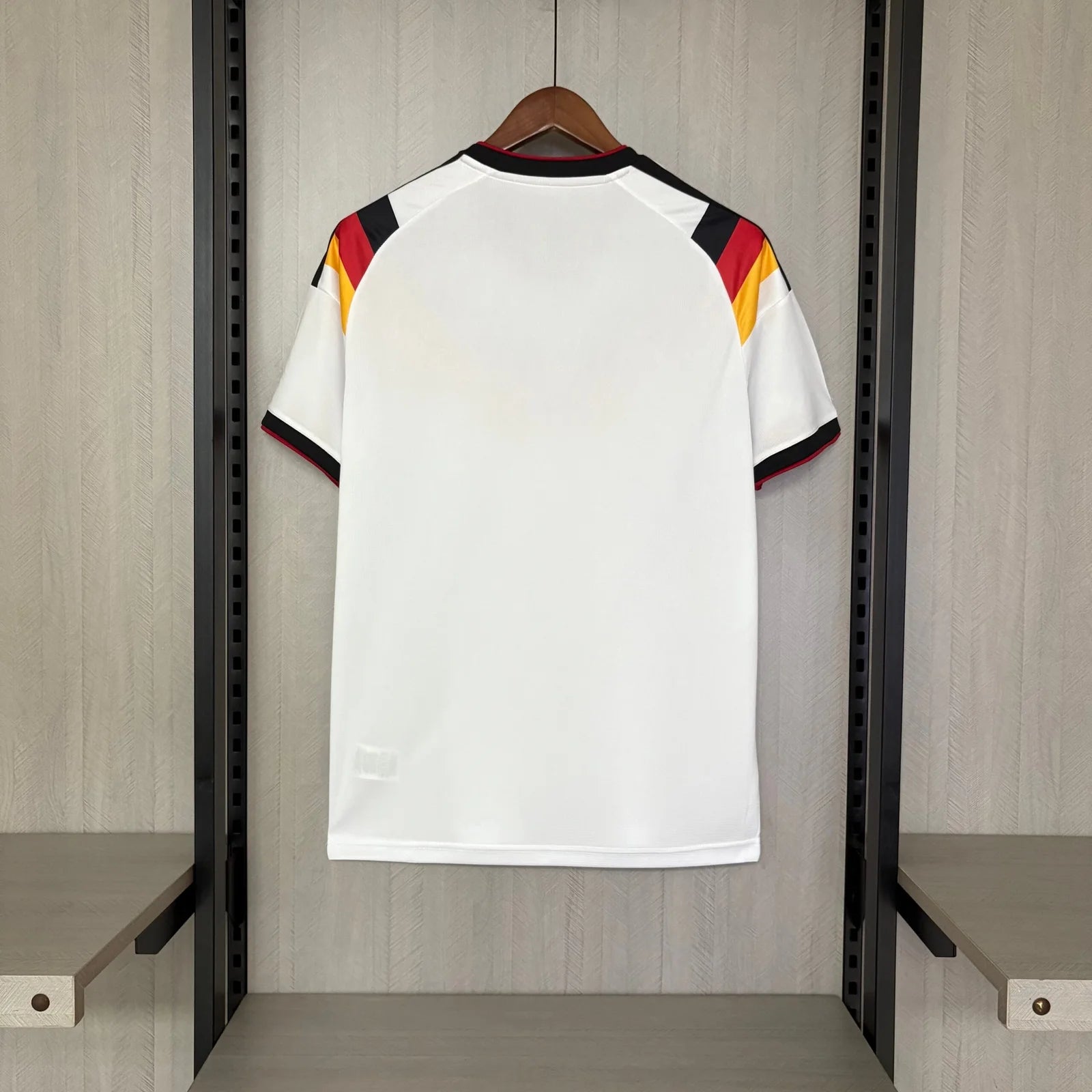 White sports jersey with red, yellow, and black accents on a hanger against a wooden panel background.
