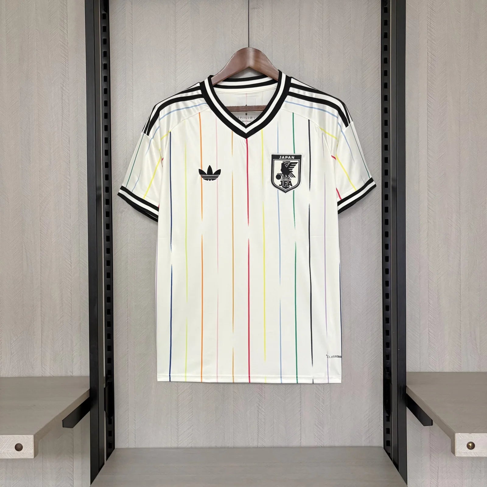 White sports jersey with colorful stripes and Adidas logo on a hanger against a wooden panel background.