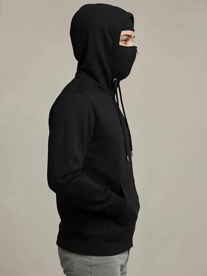 Person wearing a black hoodie with a face mask on a beige background