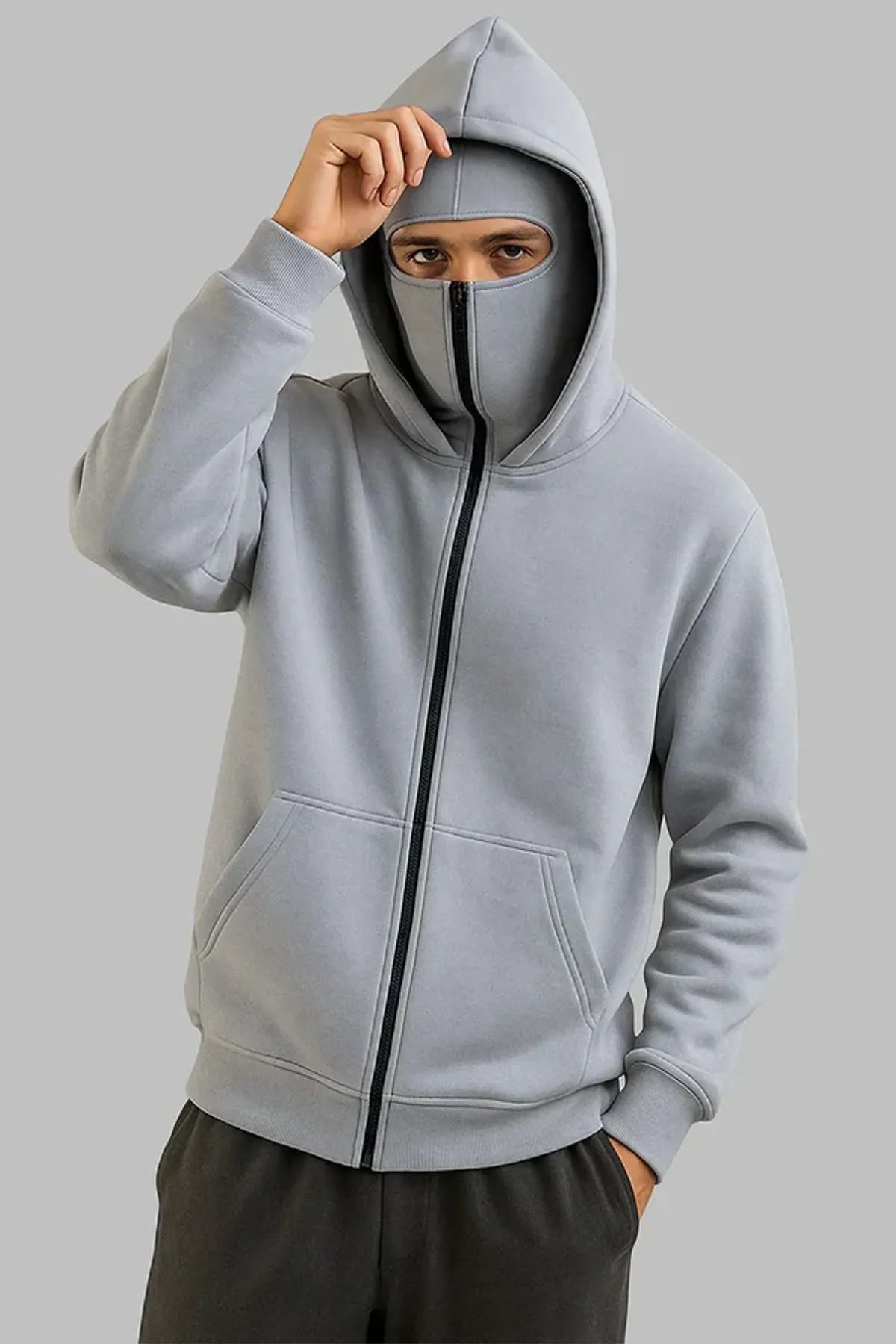 Person wearing a gray hoodie with a face mask underneath on a plain background