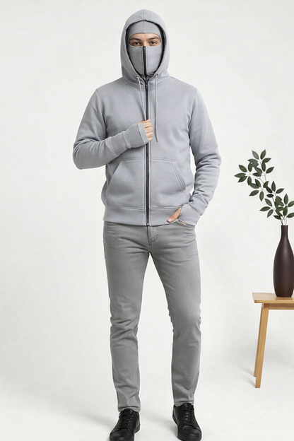 Person wearing a gray hoodie and pants on a white background with a plant and vase.