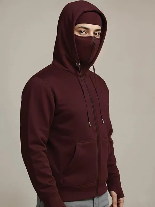 Person wearing a maroon hoodie with a face covering on a beige background