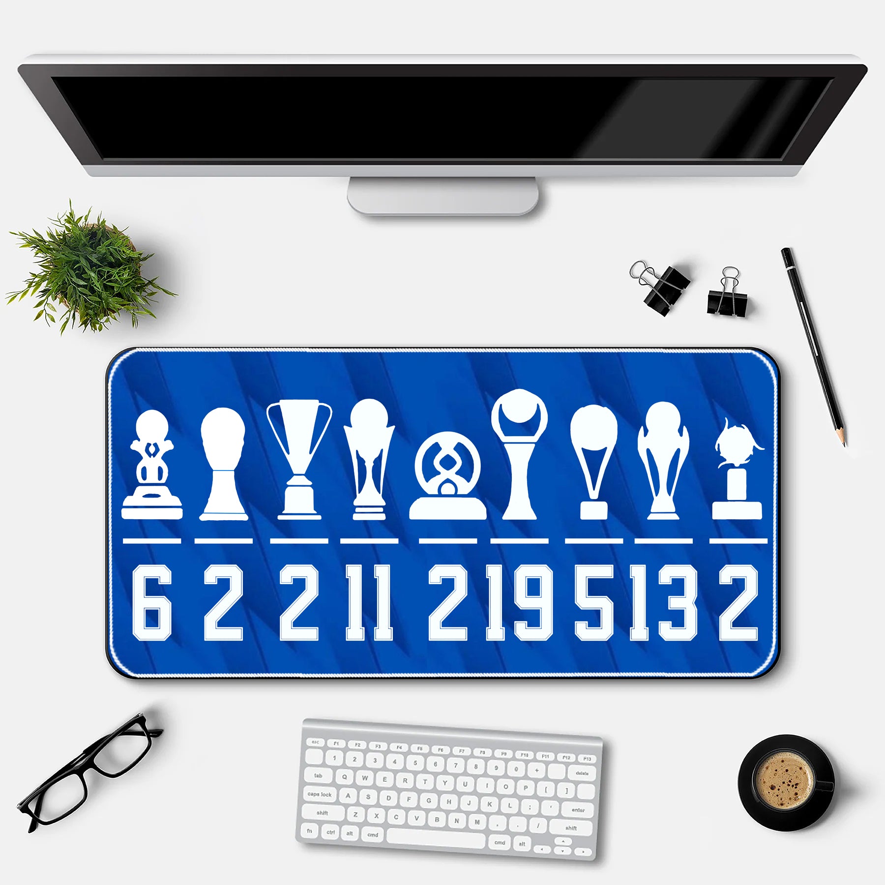 Desk setup with a blue desk mat featuring white icons and numbers, a computer monitor, keyboard, and office supplies.