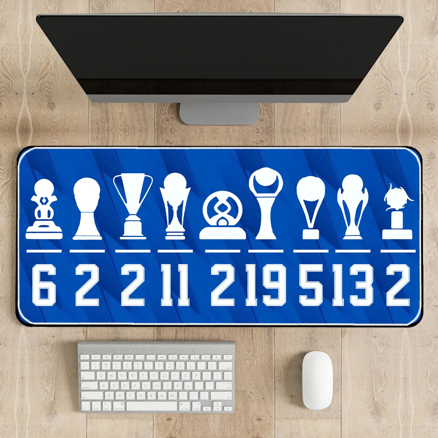 Blue desk mat with white icons and numbers on a wooden desk with a computer monitor, keyboard, and mouse.