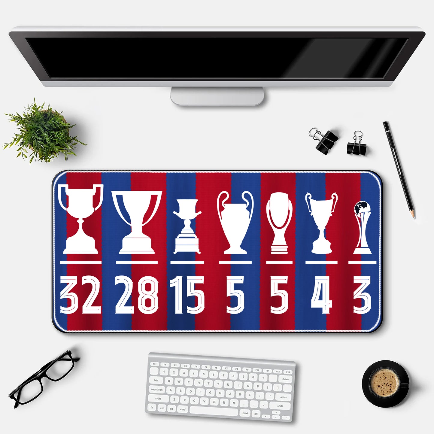 Desk setup with a decorative mat featuring trophies and numbers, a computer monitor, keyboard, and office supplies.