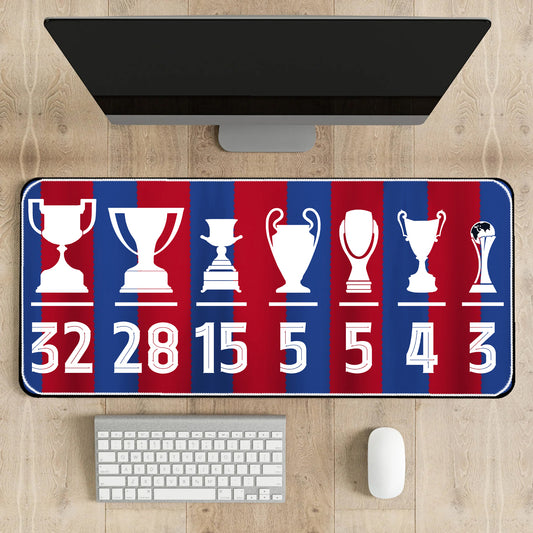 Desk setup with a large mouse pad featuring trophy designs and numbers on a wooden surface.