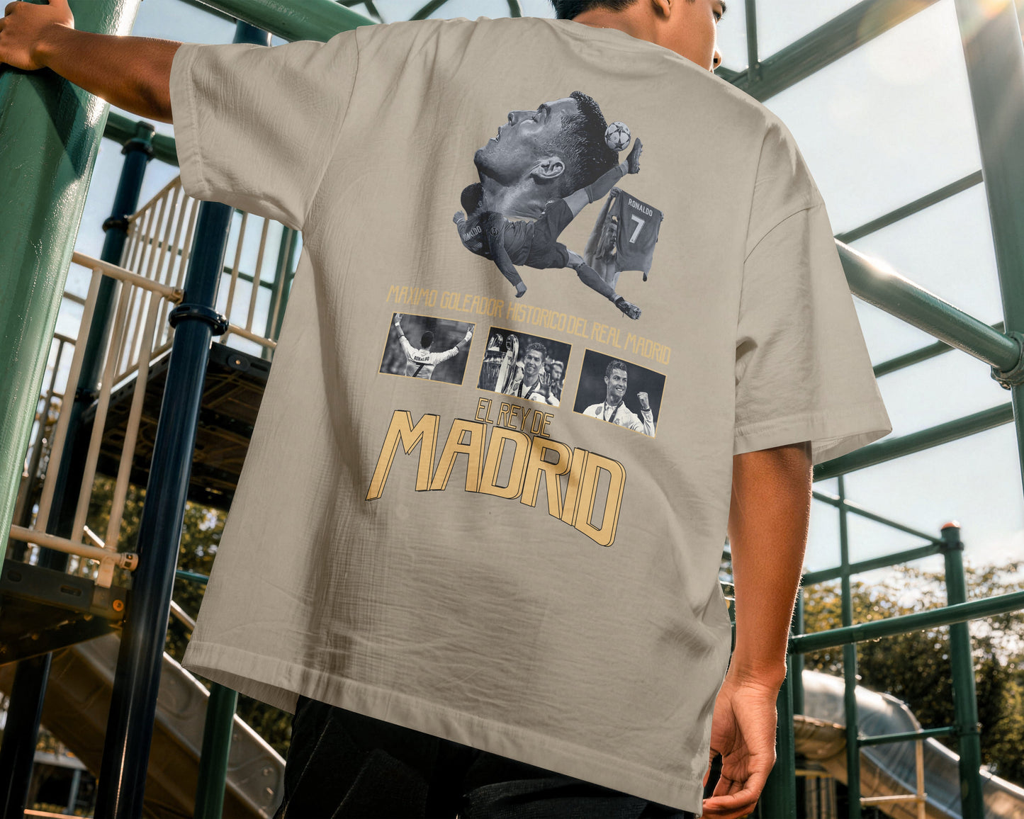 Person wearing a beige t-shirt with graphic designs and text, standing on playground equipment.