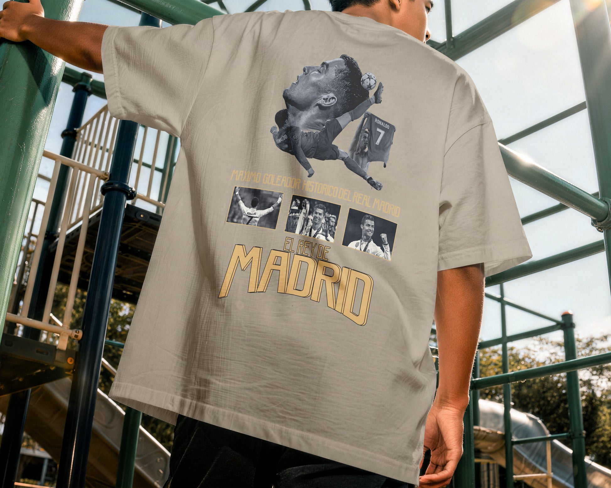 Person wearing a beige t-shirt with graphic designs and text, standing on playground equipment.