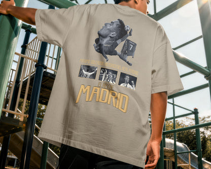 Person wearing a beige t-shirt with graphic designs and text, standing on playground equipment.