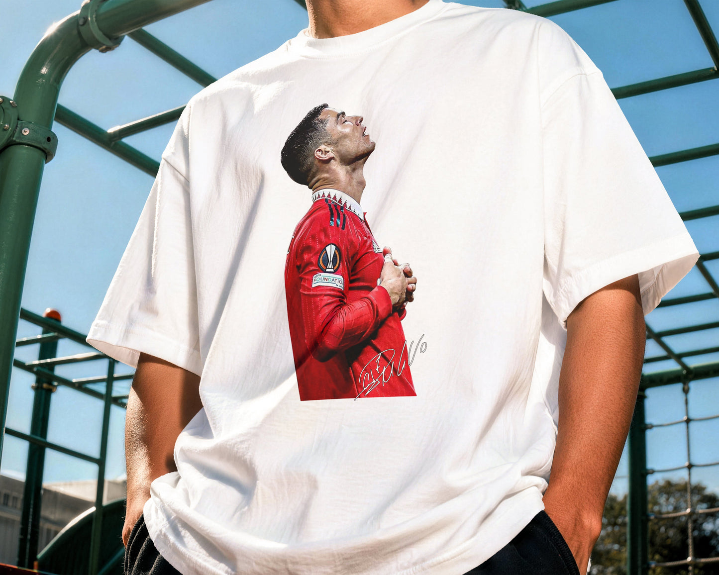 Person wearing a white t-shirt with a graphic of a person in a red outfit on a playground.