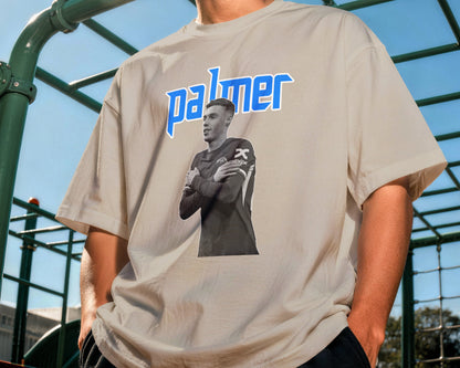 Person wearing a t-shirt with a graphic and 'palmer' text outdoors.