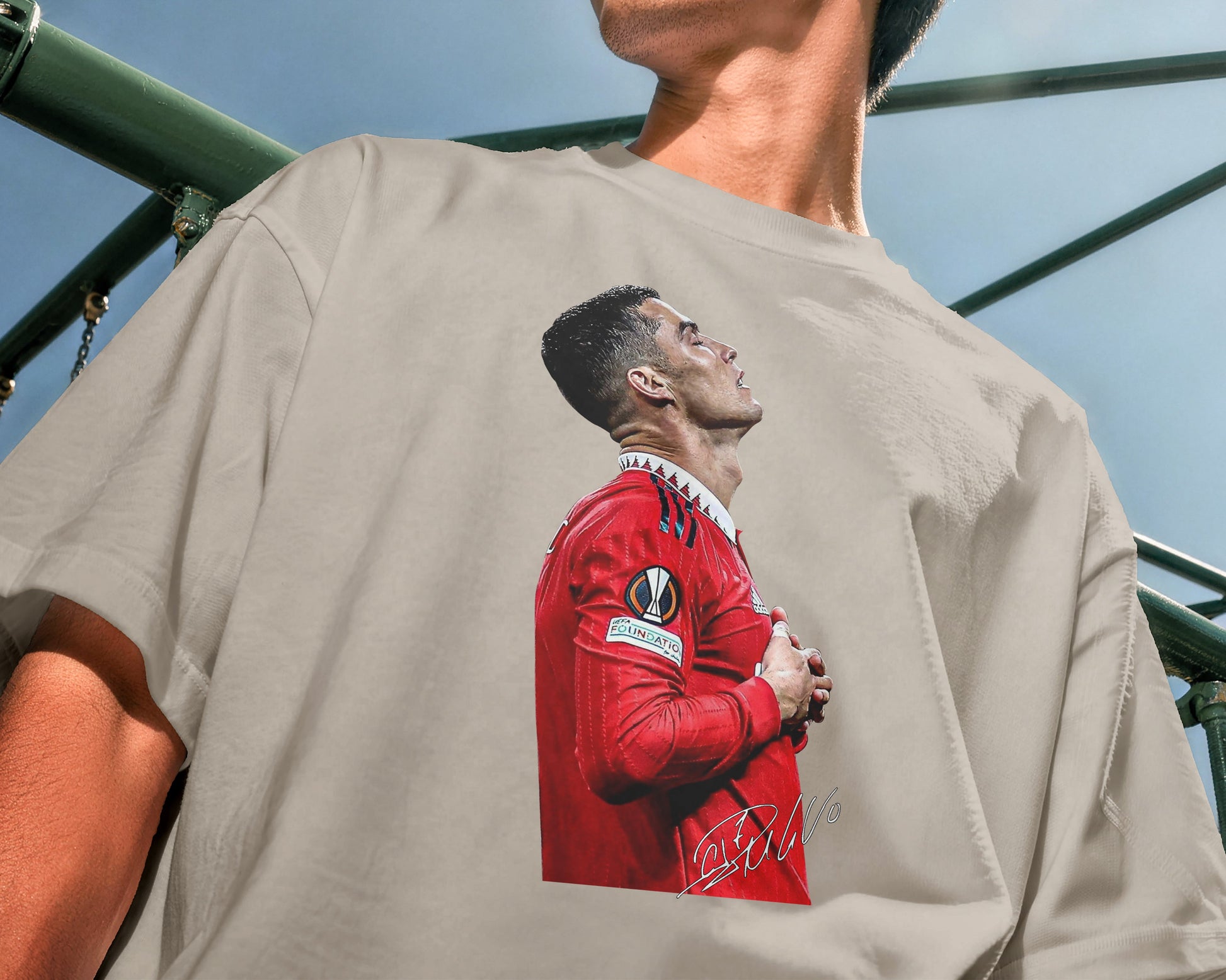 Person wearing a beige t-shirt with a graphic of a person in a red sports jersey on the back.
