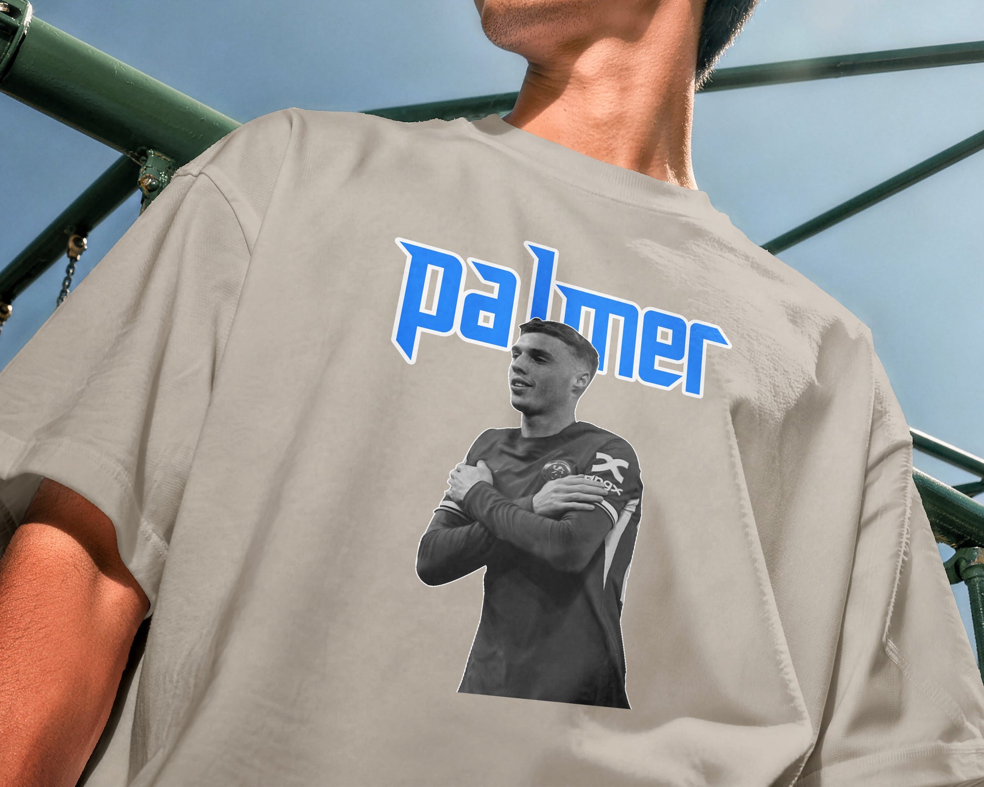 Person wearing a gray t-shirt with a graphic of a person and the word 'palmer' on the back, standing in front of playground equipment.