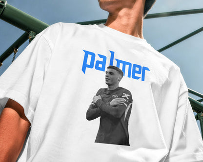 Person wearing a white t-shirt with a graphic and 'palmer' text, standing outdoors.